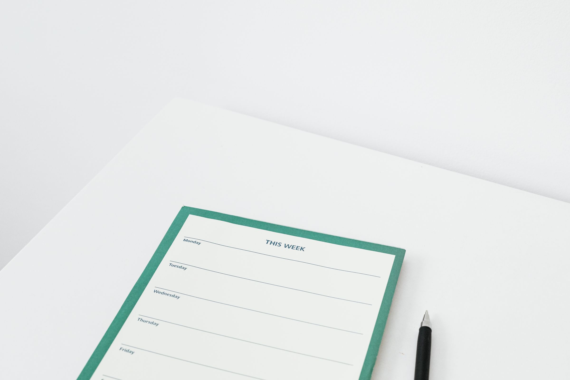 A weekly planner and pen on a white desk, for choosing a cleaning schedule