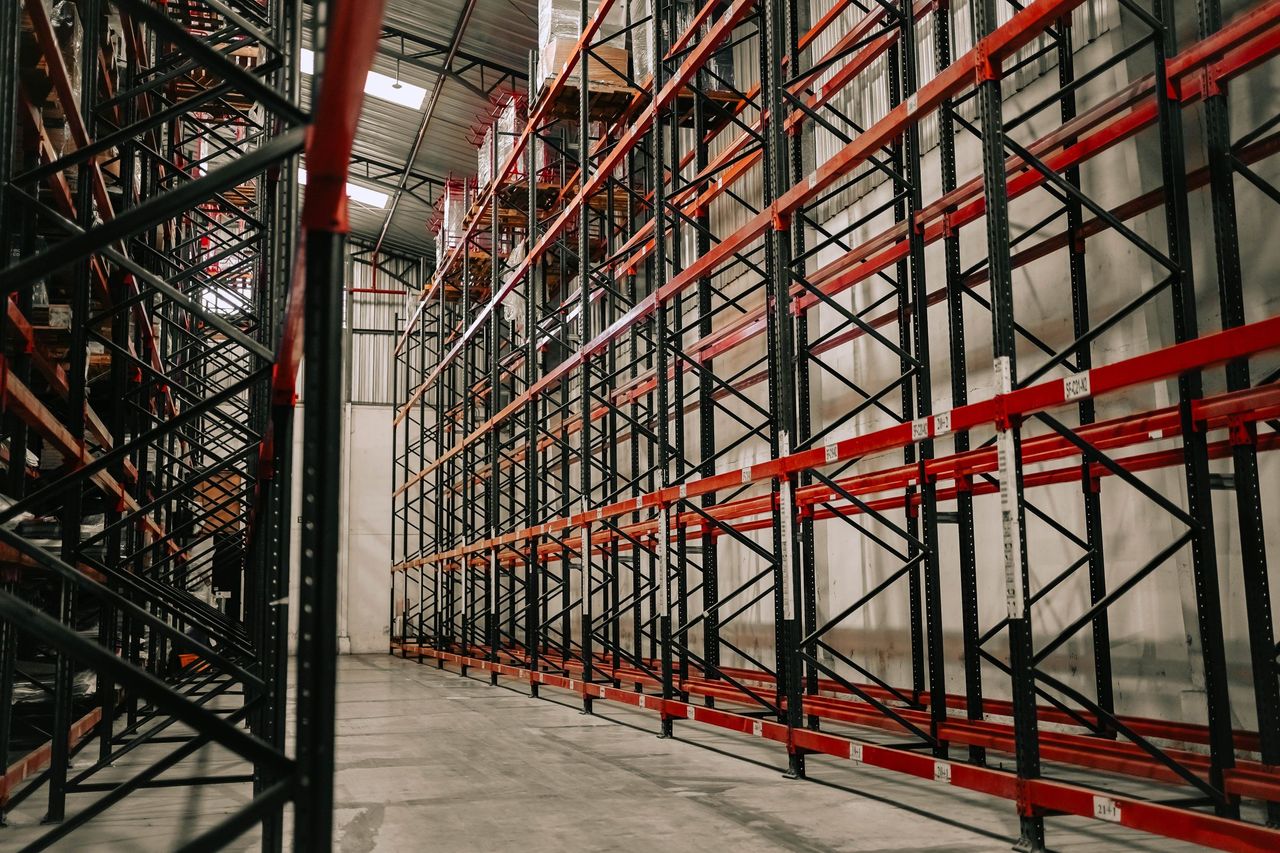A large warehouse with tall red and black pallet racks above a concrete floor