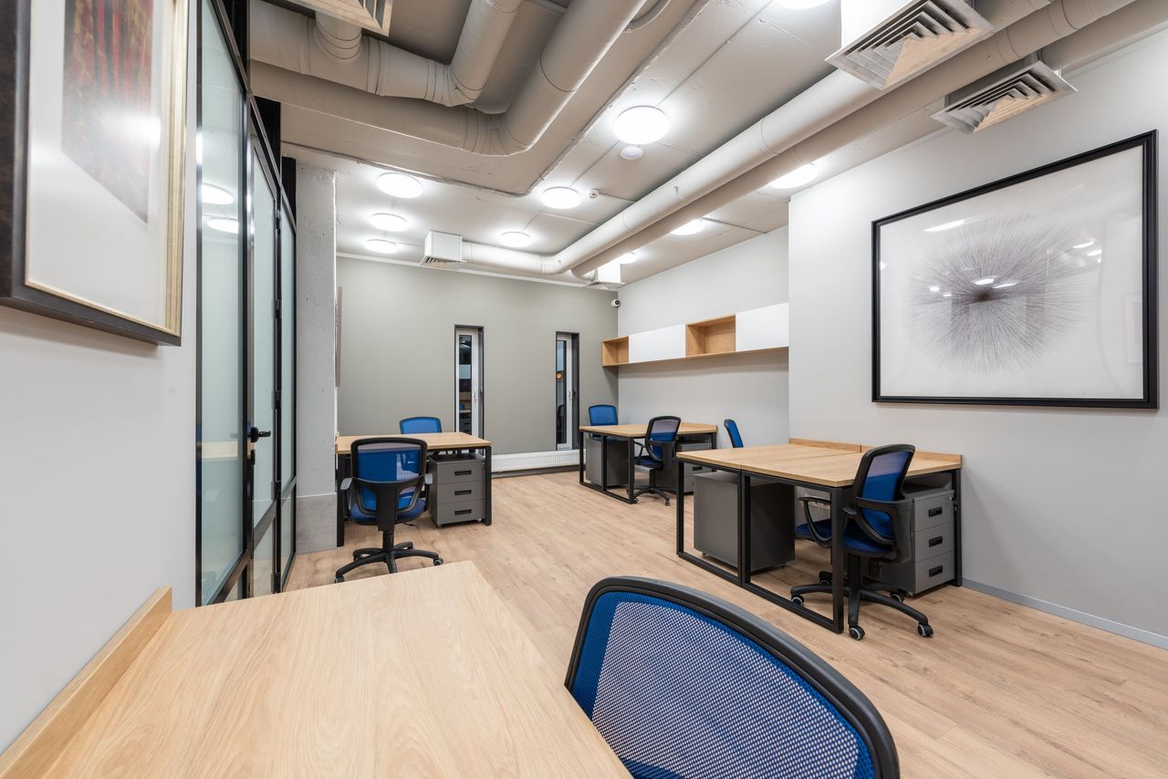 A bright open office with wood desks, blue chairs and framed artwork