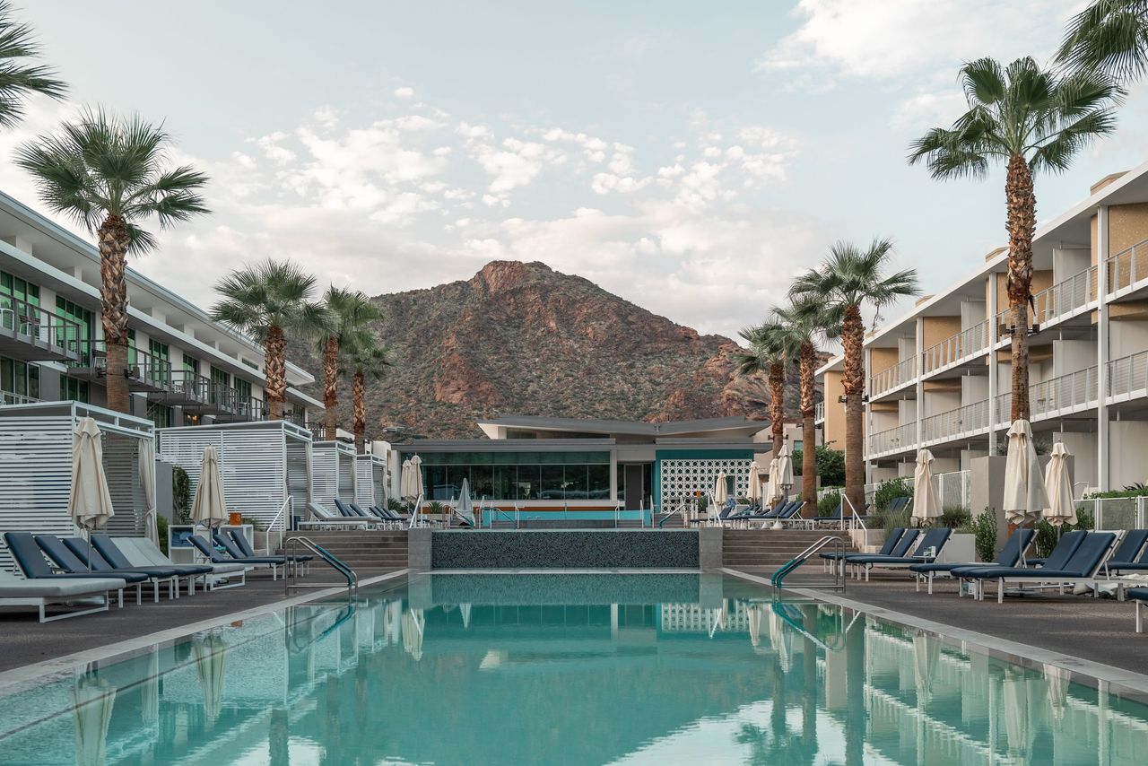 A pool courtyard with palm trees and lounge chairs between multi-story buildings with balconies