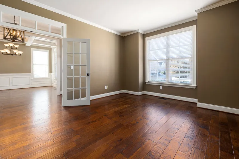 An empty living room with gleaming hardwood floors, French doors and white trim