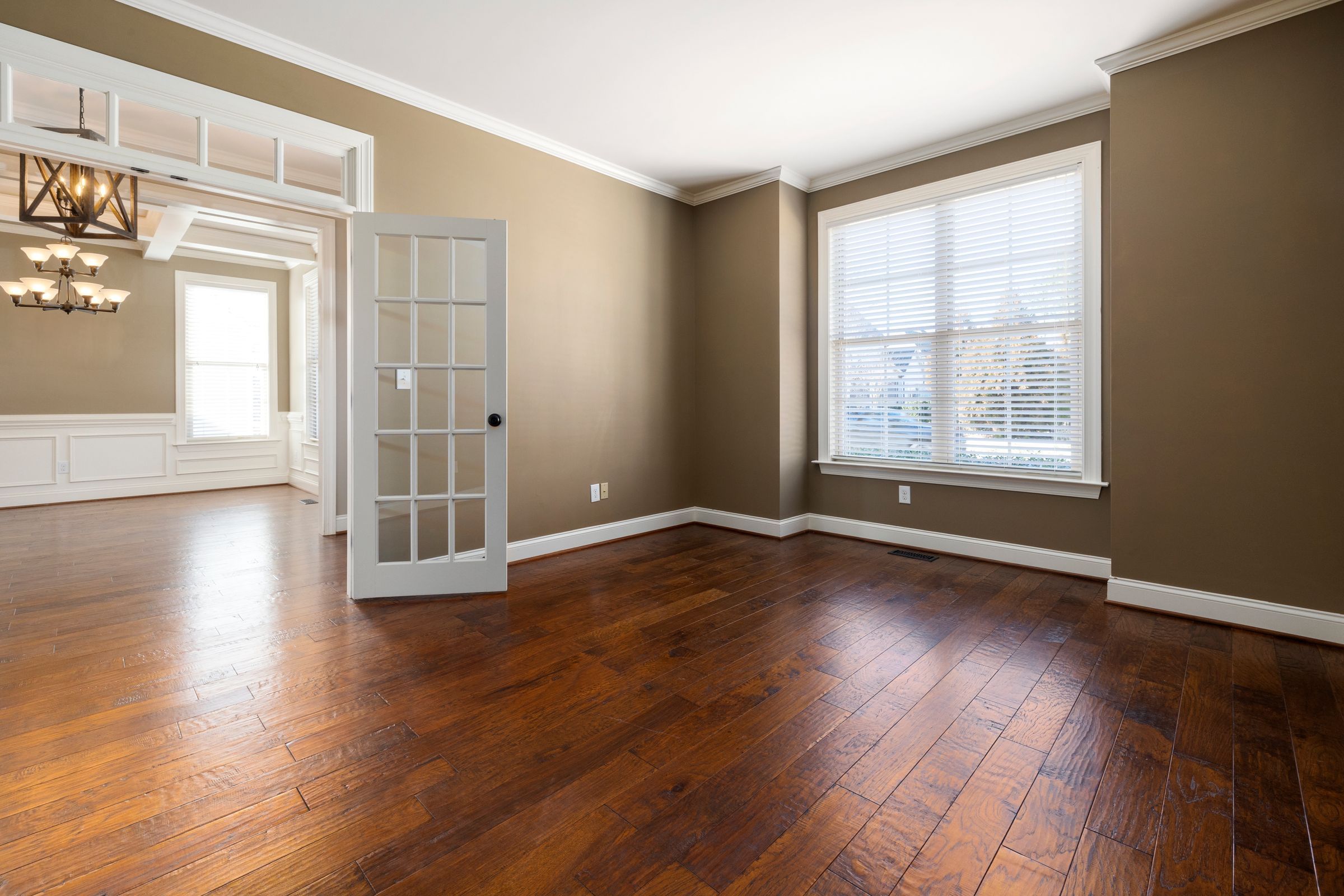 An empty living room with gleaming hardwood floors, French doors and white trim
