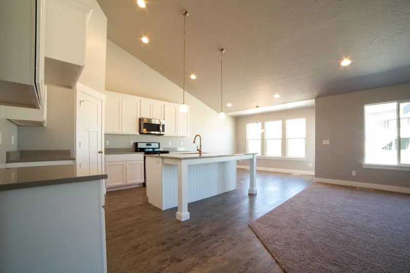 An open kitchen with a white island, white cabinets and wood floors