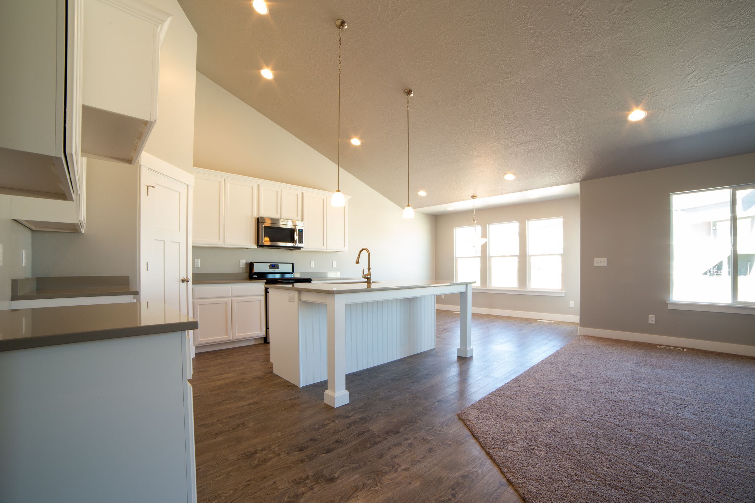 An open kitchen with a white island, white cabinets and wood floors