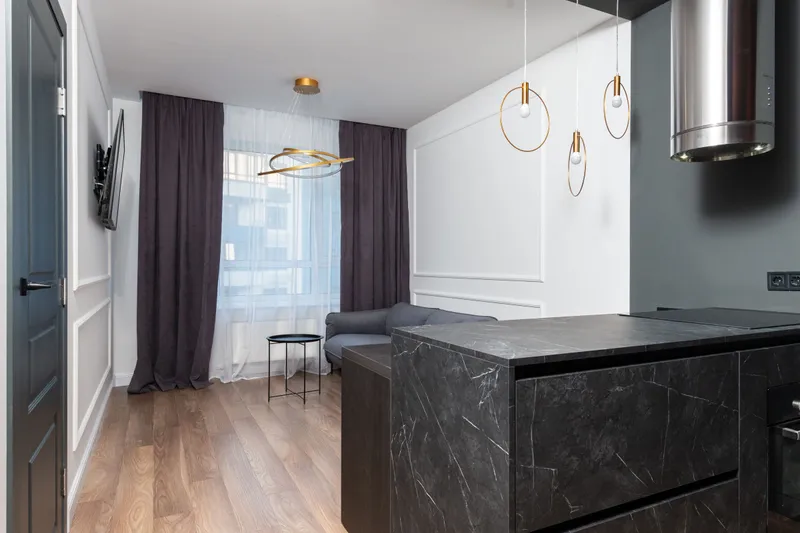 A modern apartment with wood floors, a dark marble kitchen island and long purple curtains