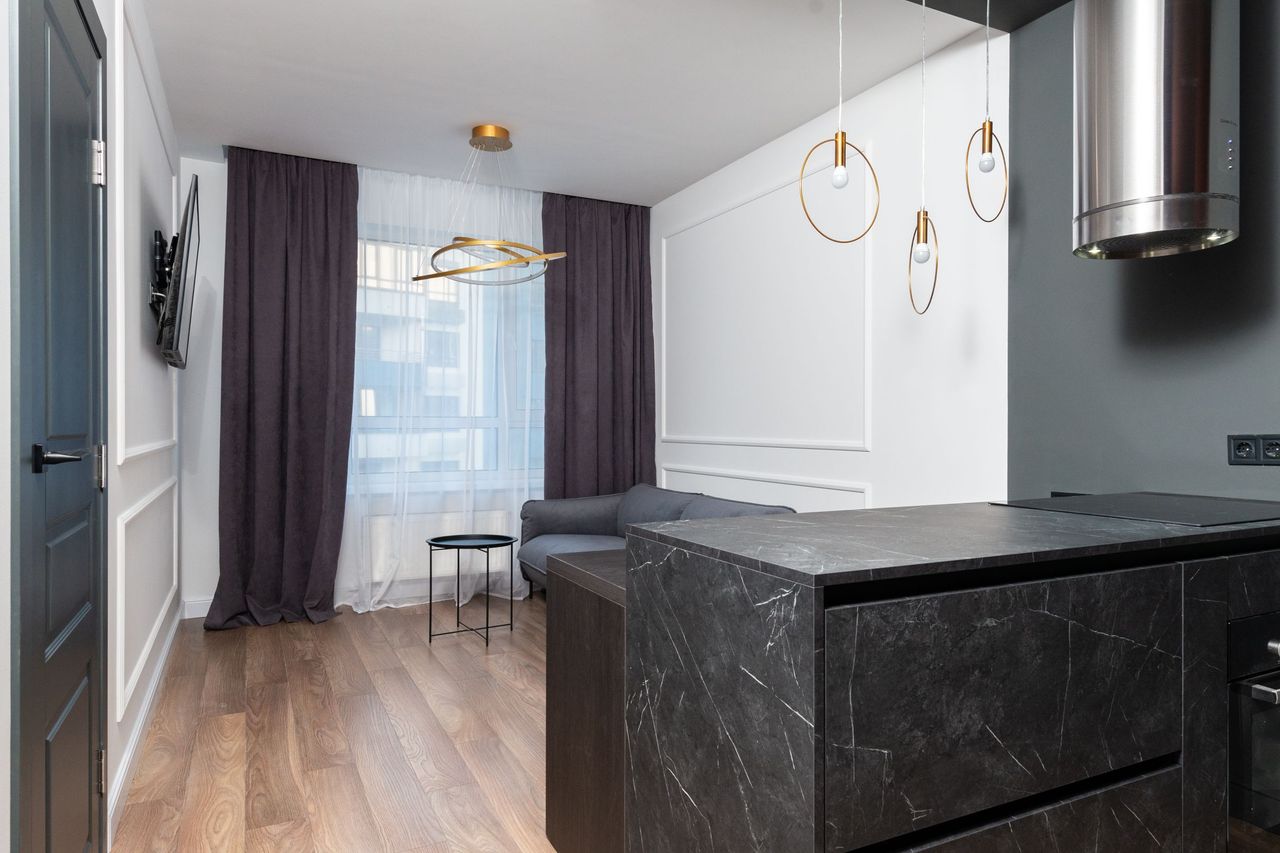 A modern apartment with a dark stone kitchen island, pendant lights and long curtains