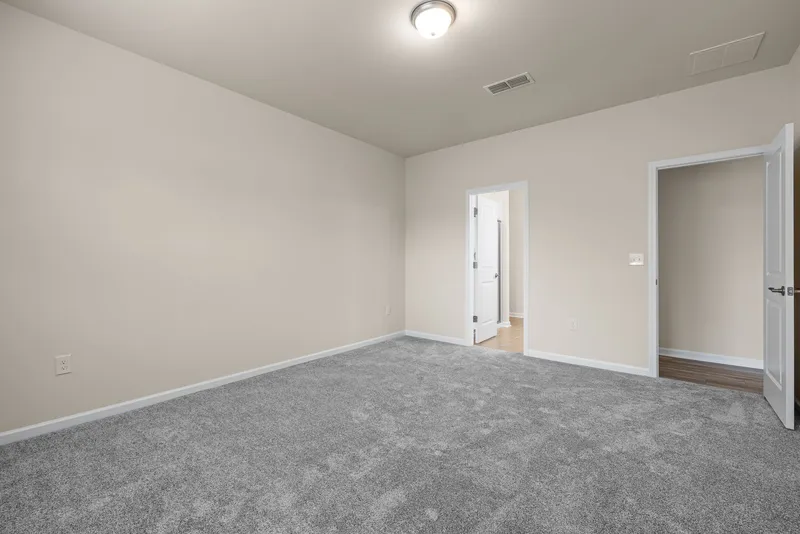 An empty room with gray carpet, white baseboards and open doors to a hallway