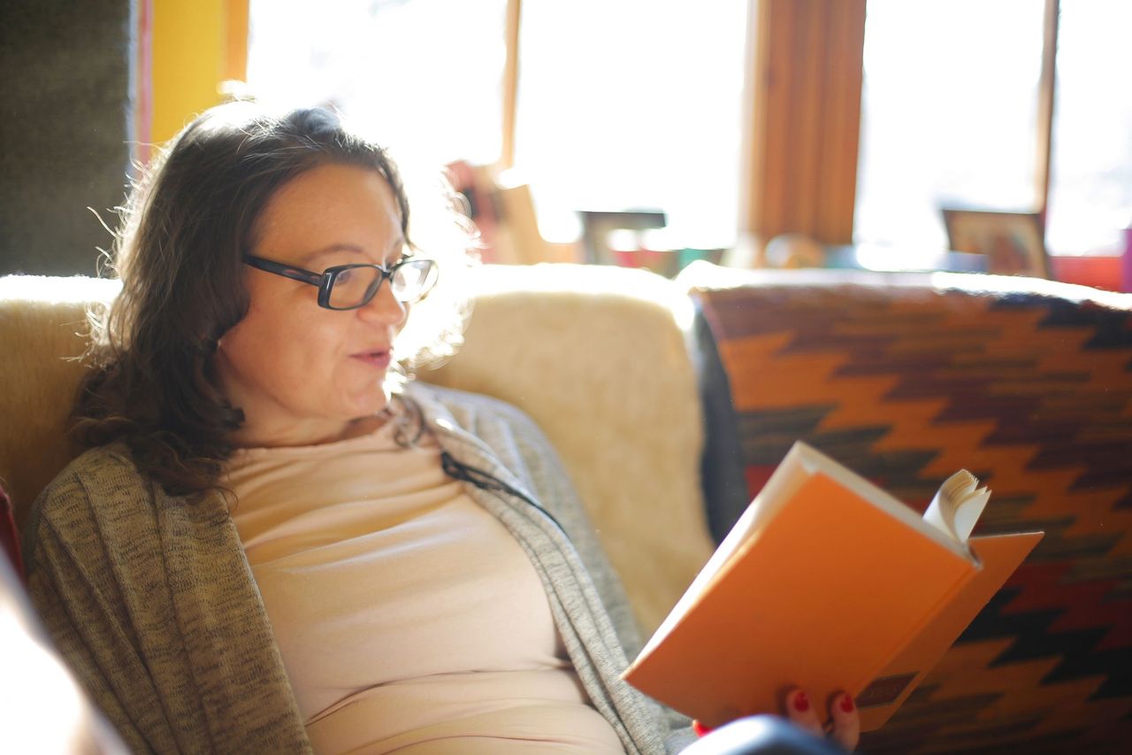 A woman reading a book in an armchair in a sunlit living room