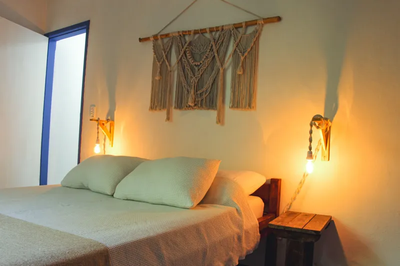 A warm bedroom with a macrame wall hanging, two pendant lamps and fresh linens